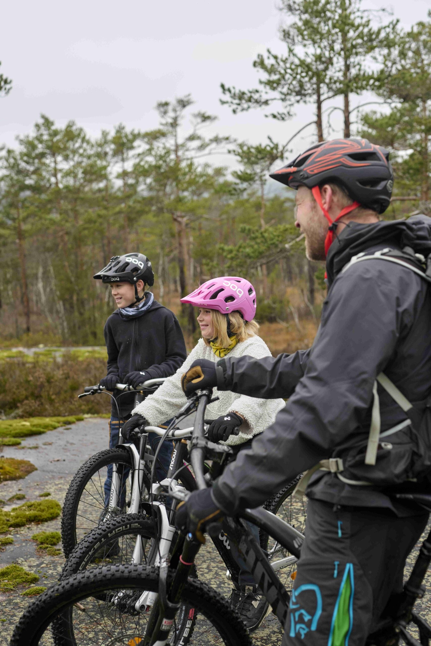 Far og to barn på sykkelen i skogen